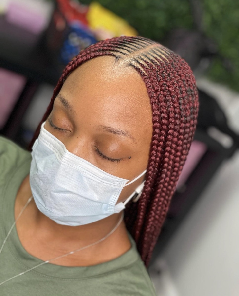 Burgundy feed-in lemonade braids swept to one side with neat baby hairs
